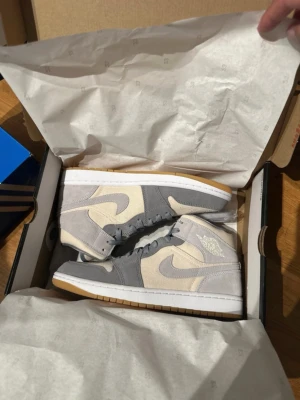 Jordan 1 coconut milk  - Nike Jordan 1 Mid coconut milk/ particle gray. sneakers i snygg grå och beige färg med vit sula och gummisula. Skorna har klassisk snörning, rund tå och är tillverkade i mocka och syntetmaterial. Perfekt för dig som gillar stilrena och neutrala färger. Aldrig använda, kvitto finns med vid köp. 