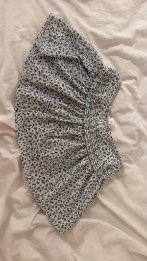 Kort blå blommig kjol från Gina Tricot - Säljer denna jätte fina kort kjol med ribbning uppe vid midjan och blå blommigt mönster. Säljer pg brist på användning, skriv för mer bilder!!🩵