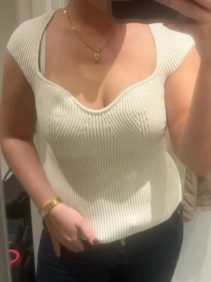 Vit ribbad topp från H&M - Säljer en snygg vit ribbad topp från H&M i storlek S. Toppen har en djup, rundad urringning och breda axelband. Materialet är stretchigt och ger en tight passform som framhäver figuren. Perfekt att styla med jeans eller kjol för en trendig look.