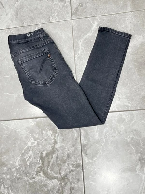 Dondup jeans - Snygga mörkgrå jeans från Dondup. Modellen är george och i skinny fit-modell. Knappgylf och smal passform som sitter tajt längs benen. Jeansen är gjorda i mjukt bomullsmaterial. Perfekta för dig som gillar en modern och stilren look. Läder patchen inuti är sönder. Storleken är i 33.