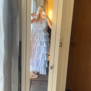 Ljusblå volangklänning med v-ringning - Säljer en drömmig ljusblå långklänning med flera lager volanger och djup v-ringning. Klänningen har ärmlös design och markerad midja, perfekt för dig som vill sticka ut. Materialet känns lätt och flowy, perfekt för sommarens alla tillfällen. Ny pris 1900 kr endast provad.