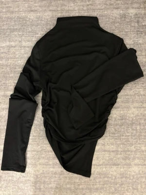 Långärmad topp  - Säljer en svart polotopp med lång ärm och tight passform. Toppen har en hög krage och är tillverkad i mjukt syntetmaterial som känns skönt mot huden. Markerar midjan väldigt fint.  