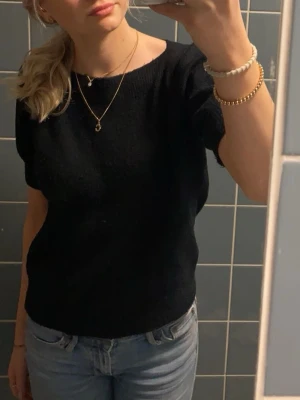 Svart stickad kortärmad tröja - Enkel och stilren svart stickad tröja med korta ärmar och rund hals. Passformen är normal och tröjan är perfekt att matcha med jeans eller kjol. Materialet känns mjukt och bekvämt mot huden.