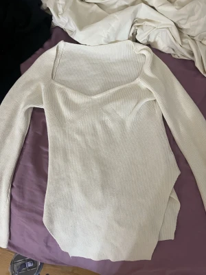 Ribbad vit långärmad topp - Säljer en ribbad vit långärmad topp med bred, fyrkantig urringning. Toppen har en figurnära passform och är tillverkad i ett mjukt stickat material som känns skönt mot huden. Perfekt att styla med jeans eller kjol för en clean look.