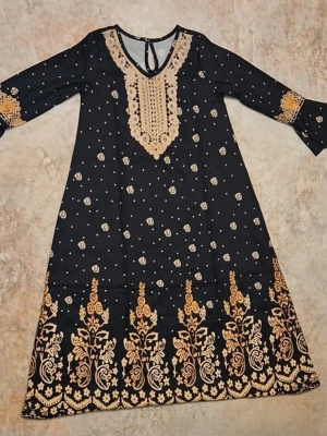 Svart långklänning med guldiga broderier - Supersnygg svart långklänning med guldiga broderier och blommönster. Klänningen har v-ringning med dekorativ spets och långa ärmar med broderade detaljer vid ärmsluten. Perfekt för dig som vill sticka ut med eleganta detaljer och unik design.