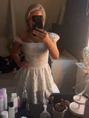 Vit blommig kortklänning med volanger - Supersöt vit kortklänning från H&M med små gula blommor, smockad överdel och puffiga offshoulder-ärmar. Klänningen har volanger i kjolen och är gjord i mjuk bomull, perfekt för sommarens alla tillfällen. Prislappen var kvar tills jag testade den för bild - då åkte den av 😅