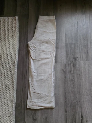 Selected femme, Beiga linnebyxor med vid passform - Snygga beiga linnebyxor med vida ben och hög midja. Byxorna har en enkel design utan synliga detaljer och är tillverkade i ett luftigt linnematerial som är perfekt för varmare dagar. Passar dig som gillar en clean och chill stil.