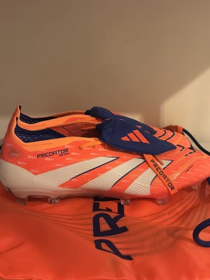 Adidas Predator CORAL BLAZE Storlek (43,44,45 - Säljer ett par Adidas Predator fotbollsskor i en riktigt fet orange färg med vita och mörkblå detaljer. Skorna har snörning, platt sula med dobbar och är gjorda i syntetmaterial med Hybridtouch-teknologi. Perfekt för dig som vill sticka ut på planen.