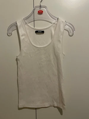 Vit linnetopp från Bikbok - Säljer en enkel och stilren vit linnetopp från Bikbok i storlek S. Toppen har rundad halsringning och är ärmlös, perfekt för varma dagar. Materialet är mjukt och skönt bomullstyg som sitter bekvämt mot kroppen.