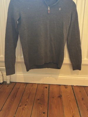 Grå stickad tröja med half zip från Morris - Säljer en mörkgrå stickad tröja med half zip och liten broderad logga på bröstet från Morris. Tröjan har långärmade ärmar och ribbade muddar vid ärmslut och nederkant. Perfekt för kyliga dagar och enkel att matcha med jeans eller chinos.