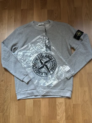 Stone Island tröja - Stilren grå Stone Island-tröja i sweatshirt-modell (hoodie utan huva). Tidlös design som passar perfekt till vardags och streetwear. Mjuk och bekväm med klassisk Stone Island-patch på ärmen.  ⭐ Skick: Mycket bra 📏 Storlek: M 🎨 Färg: Grå 👕 Passform: Normal 📦 Snabb och noggrann frakt