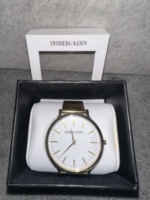 Dyrberg/kern klocka - En klocka från Dyrberg/Kern med vit urtavla och guldfärgat mesh- länk. Det är en dansk smyckesdesign mesh-armband, men ingen väst finns med. Säljs pga aldrig använd, kommer i en box och har fortfarande sin plast på. 