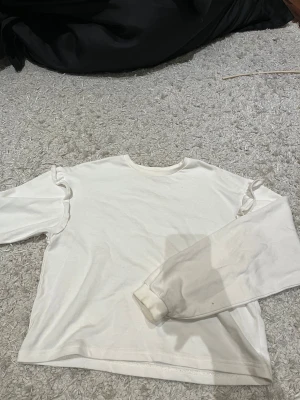 Vit långärmad tröja med volang H&M - Säljer en vit långärmad tröja från H&M i storlek 158/164. Tröjan har rund hals och snygga volangdetaljer längs axlarna som ger en extra touch. Tillverkad i mjuk bomull, perfekt för chill dagar och enkel att matcha med jeans eller kjol.
