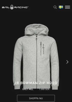 Grå hoodie från Sail Racing - Snygg ljusgrå hoodie från Sail Racing med hel dragkedja och huva. Tröjan har en bröstficka med dragkedja och logga på både bröstet och huvan. Perfekt för chill dagar och enkel att matcha med jeans eller joggers.