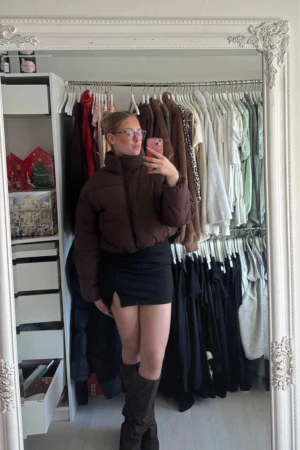 Brun croppad pufferjacka med snörning - Säljer en brun pufferjacka med croppad passform och hög krage. Jackan har dragkedja framtill och snörning i nederkant för att justera silhuetten. Materialet är syntet och jackan är perfekt för dig som gillar en chill och trendig look.