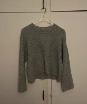 Grå stickad tröja från Gina Tricot - Mysig grå stickad tröja från Gina Tricot med rund hals och långa ärmar. Tröjan har ribbade muddar vid ärmslut och nederkant, samt en något croppad passform. Perfekt för att hålla sig varm under kyliga dagar. Använt en gång 