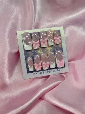 SweetFrench (S);Medium Square - Supergulliga press on-naglar i squareform med nude och handmålade vita franska tippar, dekorerade med 3D rosa rosetter och små hjärtan. Perfekt för dig som vill ha en söt och trendig look. Kommer i S: 15 mm, 11,5 mm, 12 mm, 11 mm, 9 mm 