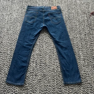 Levi's 513 blå jeans W34 L30 - Säljer ett par Levi's 513 jeans i klassisk mörkblå färg. Modellen har raka ben och fem fickor, med den ikoniska Levi's-lappen bak i midjan. Jeansen är tillverkade i slitstarkt bomullsjeansmaterial och har snygga kontrastsömmar.