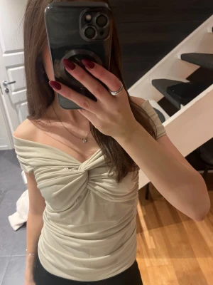 Beige omlott offshoulder topp - Säljer en beige omlott topp med snygg twistad detalj framtill. Toppen är offshoulder och med ett stretchigt material. Knappt använd och i väldigt bra skick.