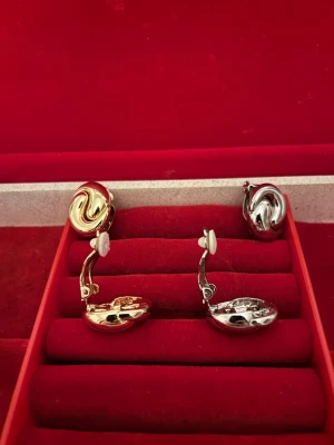 Två par swirlade clip-on örhängen - Säljer två par retro swirlade clip-on örhängen, ett par i blank guldton och ett par i blank silverton. Båda har en rundad, snurrad design som ger cool 90-talsvibe. Perfekt för dig som vill sticka ut med metallic-accessoarer utan hål i öronen.