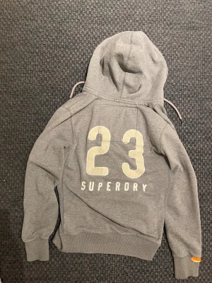 Sällsynt Vintage SuperDry zip hoodie med tryck på ryggen - Säljer nu denna sjukt snygga och eftertraktade vintage SuperDry zip hoodie! Passar perfekt nu till höst och vinter ❄️ Trycket på ryggen gör denna hoodie till en unik piece som du bara måste ha i garderoben🤩 Skriv vid funderingar 🤝📲