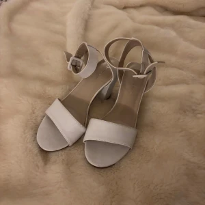 Vita sandaler med blockklack - Stilrena vita sandaler med bred rem över tårna och justerbart spänne runt ankeln. Skorna har en stabil blockklack och öppen tå. Lite smuts finns på skorna som lätt kan torkas av (vilket jag kommer göra innan jag skickar dem)