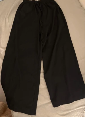 Svarta wide byxor med snörning - Säljer ett par svarta byxor med breda ben och skön passform. De har elastisk midja med snörning och är tillverkade i ett mjukt tyg som känns chill. Perfekta för dig som gillar loose och avslappnad stil.