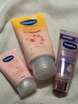 Vaseline ansiktskrämer och ampoule - Tre olika ansiktskrämer från Vaseline: en rosa Healthy Hands Stronger Nails handkräm (75ml), en stor rosa och gul ansiktskräm (300ml) samt en lila GlutaGlow Ampoule Bright & Smooth med glansigt lock. Perfekt för dig som vill ha återfuktad och mjuk hud.