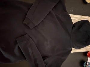 Svart hoodie från Sail Racing - Svart hoodie från Sail Racing med hel dragkedja och huva. Tröjan har en bröstficka med dragkedja och logga på både bröstet och huvan. Mjuk insida och ribbade muddar vid ärmslut. Perfekt för chill eller när du vill ha en clean look.