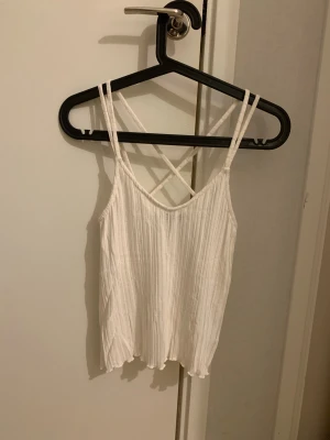 Vit ribbad linnetopp - Säljer ett linne/topp i storlek XXS i en krämvit färg. Toppen har smala axelband som korsas i ryggen och ett ribbat tyg. Materialet är mjukt och lätt, perfekt för varma dagar. Den har en loose passform med vågig kant nedtill. Har använt fåtal gånger🩷