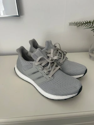 Grå Adidas Ultraboost sneakers - Snygga Adidas Ultraboost sneakers i ljusgrått med stickad ovandel och klassiska tre ränder på sidan. Skorna har en vit Boost-sula för extra komfort och svart yttersula. Perfekta för dig som gillar stilrena och sportiga sneakers med modern känsla.