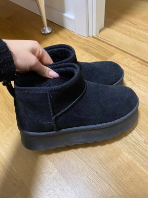 Svarta boots från Boohoo i mocka - Svarta boots från Boohoo med rund tå och platt sula. Skorna är i mjuk mocka med fluffigt foder på insidan och har en enkel, stilren design. Perfekta för kyliga dagar när du vill ha både värme och stil.