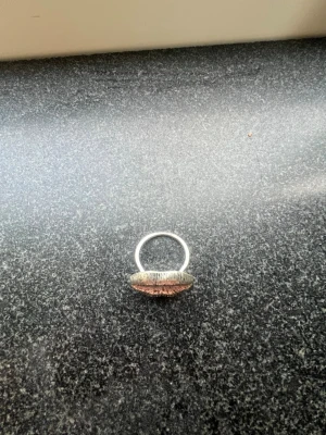 Unik silverring med kopparfärgad detalj - Cool ring i silverfärgat metall med en stor, rund dekoration i kopparfärg. Dekorationen har en texturerad yta som ger ringen en rustik och handgjord känsla. Perfekt för dig som gillar statement-smycken och vill sticka ut.