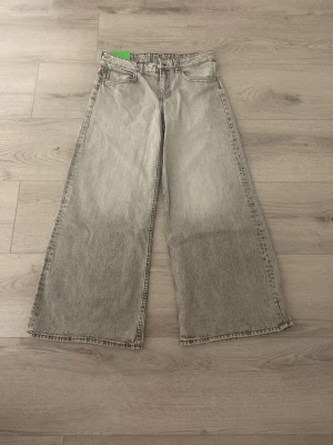 Grå wide jeans från Monki - Säljer ett par gråa wide jeans från Monki med medel hög midja och raka, vida ben. Klassisk femficksmodell i mjuk bomullsdenim med en snygg tvättad look. Perfekta för dig som gillar avslappnad och trendig stil.Helt nya aldrig använda