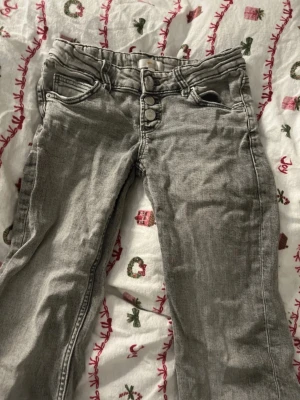 Gråa utsvängda jeans med knappar - Snygga gråa utsvänga  jeans med flera knappar i midjan och klassiska fickor. Jeansen har en smal passform och är perfekta för en trendig vardagslook. Materialet är mjukt och stretchigt jeans-tyg.
