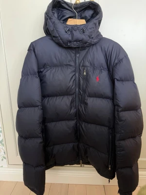Mörkblå dunjacka Polo Ralph Lauren - Snygg mörkblå dunjacka/vinterjacka från Polo Ralph Lauren. Jackan är i 8/10 skick då den är lite smutsig. Annars är den i jättebra skick och helt utan hål (se bilderna).Perfekt för den kalla vintern som nyss kommit. Hör av er för fler bilder eller frågor. Pris kan diskuteras.