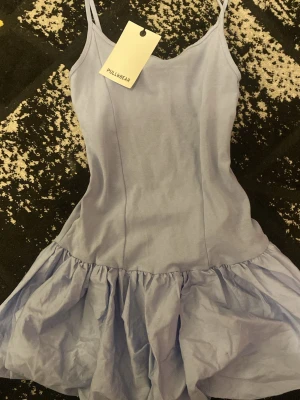 Ljusblå klänning från Pull&Bear - Ljusblå klänning från Pull&Bear med smala axelband och volangig kjol. Klänningen har en figurnära överdel och är tillverkad i ett mjukt material som känns skönt mot huden. HELT OANVÄND MED PRISLAPP KVAR. 