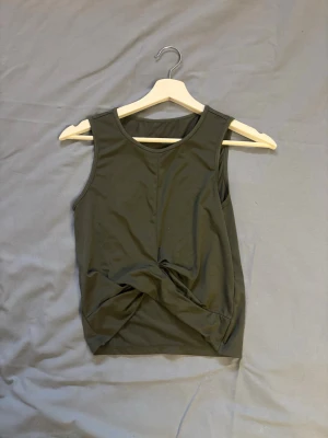 Mörkgrön twistad linnetopp - Snygg mörkgrön sporttopp med twistad detalj framtill. Toppen är ärmlös och har en rund halsringning. 