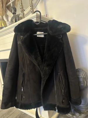 Svart pälsjacka med dragkedjor - Snygg svart pälsjacka från Stradivarius med stora slag, fuskpälsfoder och detaljerade dragkedjor framtill. Jackan har bälte i nederkant och långa ärmar, perfekt för kalla dagar. Stilsäker och trendig look.