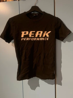 Svart Peak Performance t-shirt - Säljer en svart t-shirt från Peak Performance med stor vit logga på bröstet. Klassisk rund hals och korta ärmar. Perfekt till dig som gillar sportig och enkel stil. Tillverkad i mjuk bomull för skön känsla hela dagen.