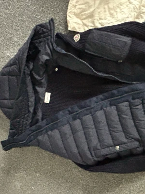 Mörkblå dunjacka från Moncler - Snygg mörkblå dunjacka från Moncler med quiltad design och huva. Jackan har dragkedja framtill och Moncler-logga på ärmen. Tillverkad i polyester och dun, perfekt för kyliga dagar. Klassisk passform och tidlös look.