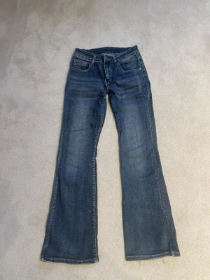 Lågmidjade blå bootcut jeans med klassisk tvätt - Snygga blå bootcut jeans med klassisk tvätt och femficksmodell. Jeansen har en låg midja och raka ben som går ut något nedtill för en retroinspirerad look. Perfekta till sneakers eller boots och tillverkade i slitstarkt denimtyg.