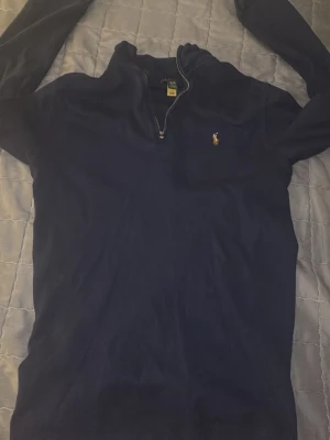 Marinblå zip-jacka från Polo Ralph Lauren - Snygg marinblå zip-jacka från Polo Ralph Lauren med klassisk halv dragkedja och broderad logga på bröstet. Tillverkad i mjukt bomullsmaterial och har långärmad design. Perfekt för en stilren och avslappnad look. Köpt från Zalando 2024