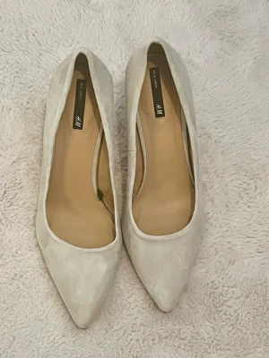 Vintage pumps i mocka från H&M - Stilrena pumps från H&M i ljusbeige mocka med spetsig tå och smal hög klack. Skorna har en elegant siluett och är perfekta för dig som gillar klassisk och enkel design. Vintage klackskor, aldrig använda, kommer i originalpåse och lappen kvar 👠