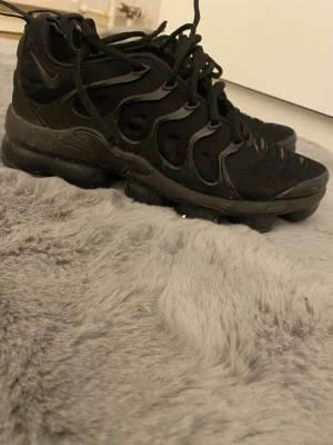Svarta Nike Air Vapormax sneakers - Säljer ett par svarta Nike Air Vapormax sneakers med cool design och synliga luftbubblor i sulan. Skorna har snörning och en unik struktur på ovandelen som ger en modern vibe. Perfekta för dig som gillar streetwear och sportig stil.