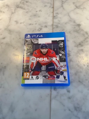 NHL 21 till PS4 - NHL 21 till PlayStation 4, ishockeyspel med omslag i blå plastfodral. Spelet har en omslagsbild med en spelare i röd hockeytröja och innehåller ligor som SHL och Liiga. Perfekt för dig som gillar sportspel och hockey.