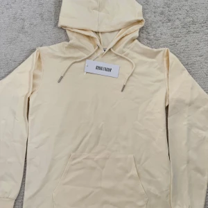 Ljusbeige hoodie från Bubbleroom - Snygg ljusbeige hoodie från Bubbleroom med huva och snörning. Tröjan har en klassisk känguruficka framtill och långa ärmar. Tillverkad i en mjuk mix av viskos, polyamid och elastan för en skön känsla. Perfekt för en chill och avslappnad stil.