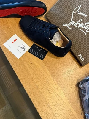 Mörkblå sneakers från Christian Louboutin - Snygga mörkblå sneakers från Christian Louboutin med klassisk röd sula. Skorna har rund tå, snörning och är tillverkade i mocka för en lyxig känsla. Perfekta för dig som vill sticka ut med stilrena detaljer och exklusiv design.