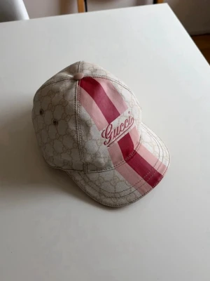 Gucci keps  - JÄTTEsnygg keps från Gucci i beige med klassiskt GG-mönster och breda röda och rosa ränder framtill.