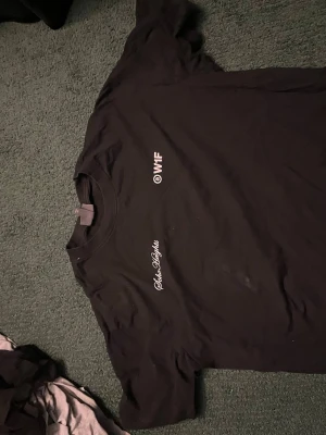 Svart t-shirt med tryck från Soho Nights - Cool svart t-shirt från Soho Nights med vit text på bröstet där det står '@WTF' och 'Soho Nights'. Klassisk passform och rund halsringning. Perfekt för dig som gillar streetwear och vill ha något enkelt men ändå med attityd.